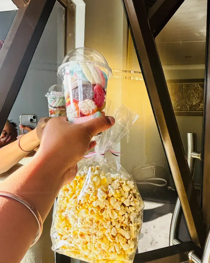 A cup of layered marshmallows and jellies beside a ribboned bag of popcorn