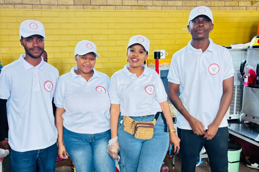 Four Sedi Events staff in branded white polo shirts and caps beside the machines